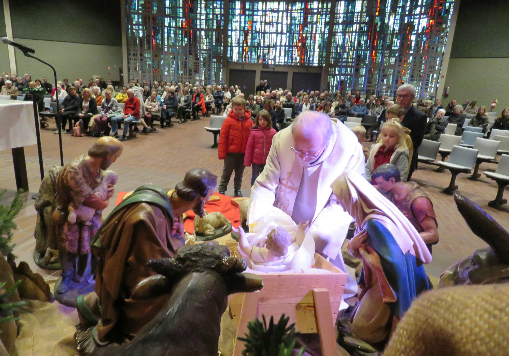 Priester Paul Scheelen legt het Kindje samen met andere kinderen in de kribbe van de kerststal